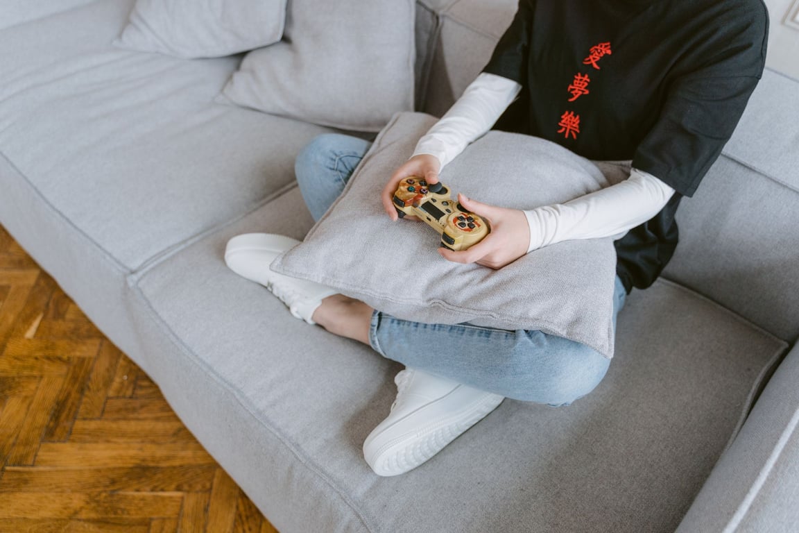 Person sitting on a grey couch holding a video game controller, focusing on arm and hand support while gaming