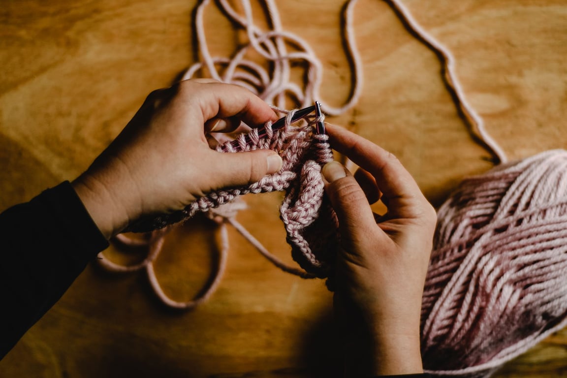 pink yarn, wooden table, hands knitting, close up, cozy indoor setting