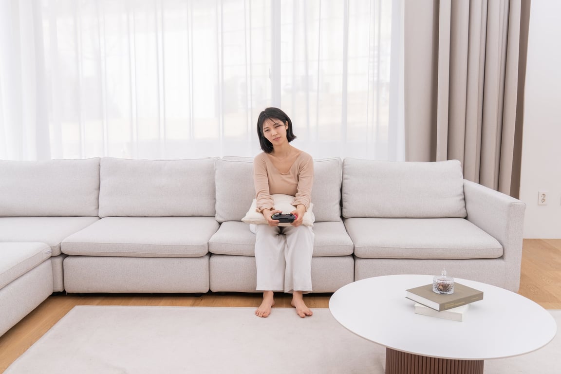 게임 컨트롤러를 들고 소파에 앉아 흰색 펌플렉스 레벨업쿠션을 팔 밑에 둔 사람