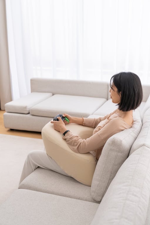 소파에 앉아 베이지색 펌플렉스 레벨업쿠션에 팔을 resting하며, 일상 활동 중 어깨 긴장 완화를 위해 전완부를 지지하는 제품 사용법을 시연하는 모습