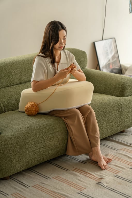 緑色のソファに座り、ベージュのクッション上で編み物をする女性
