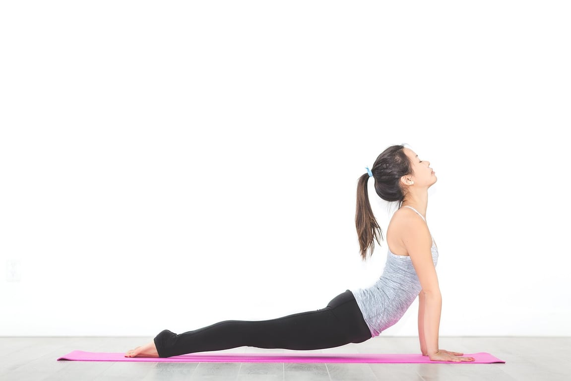 하얀 벽 배경의 실내에서 분홍색 요가 매트 위에 앉아 코브라 자세(Cobra Pose)로 등部和 목 부위를 스트레칭하는 여성