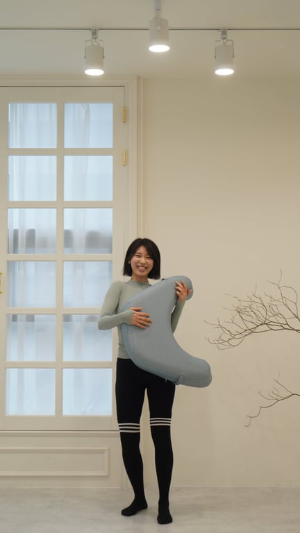 明るいスタジオ背景でショートヘアの女性が薄いブルーグリーンのレベルアップクッションを両手で抱えて明るく笑っている様子
