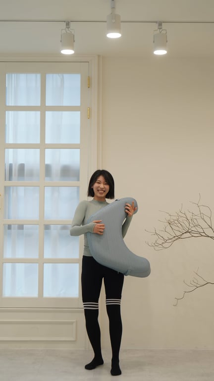ライトブルーのレベルアップクッションを両手で正面に向けて持ち、明るく微笑む20代の女性モデル