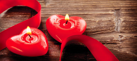 Dos velas rojas con forma de corazón encendidas y lazo rojo