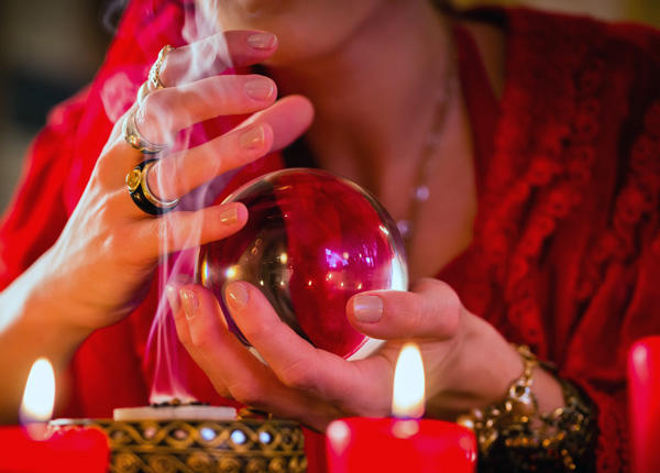 Manos sobre una bola de cristal entre velas encendidas