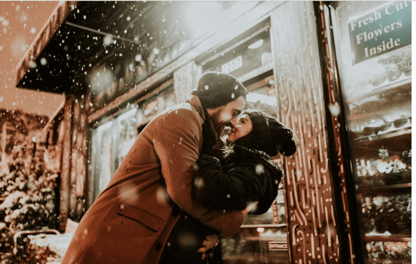 Pareja besándose bajo la nieve frente a una floristería