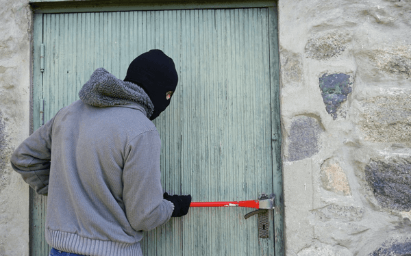 Ladrón con pasamontañas forzando una puerta con una palanca