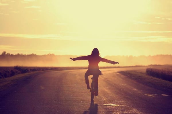 Silueta en bicicleta por una carretera al atardecer, brazos abiertos