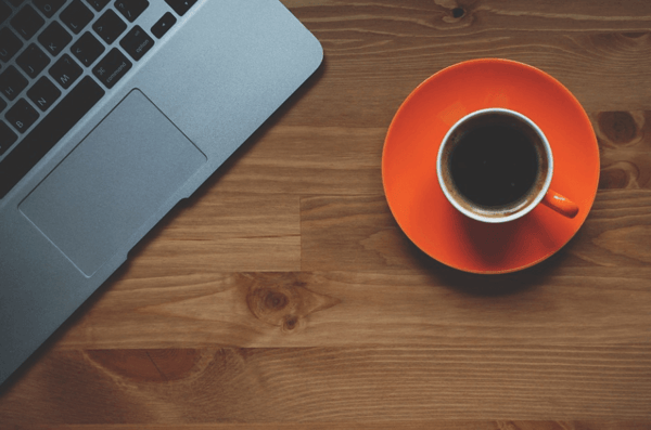 Portátil y taza de café naranja sobre un escritorio de madera