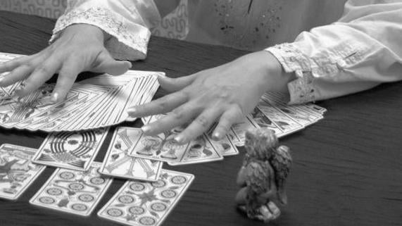 Dos manos extendiendo una baraja de tarot de Marsella sobre una mesa oscura
