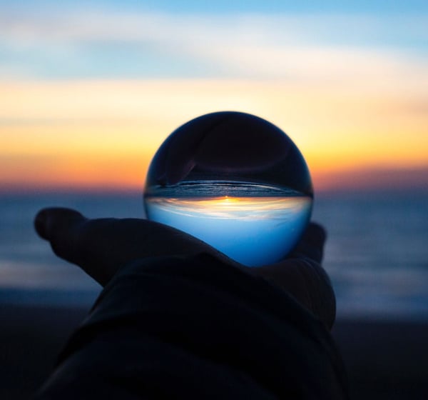 Mano sosteniendo una bola de cristal frente al atardecer