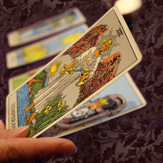 Mano sosteniendo la carta de la Templanza sobre un mantel oscuro
