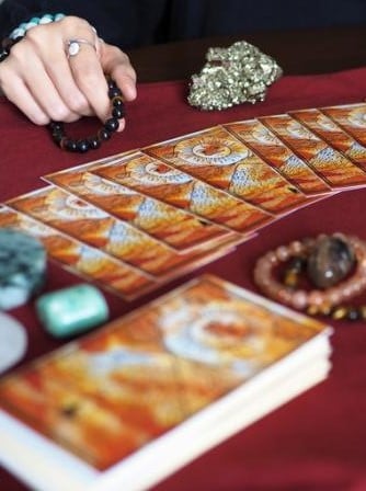 Mano con pulseras sobre cartas de tarot naranjas en tela roja