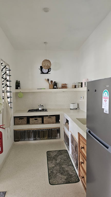 Narrow bright kitchen with hob, counters, woven storage baskets and refrigerator