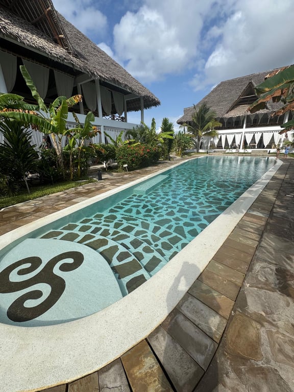 The shared resort pool beside tropical plants and a thatched pavilion