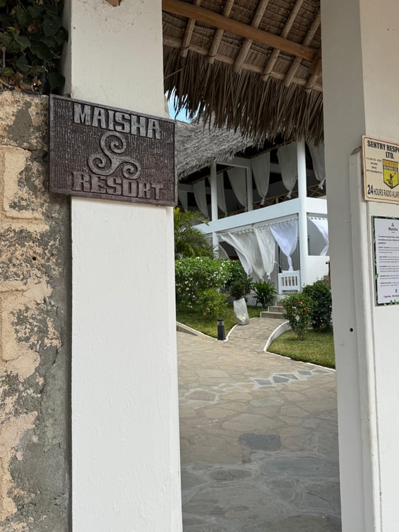 Wooden Maisha Resort sign at a thatched entrance with a stone path beyond