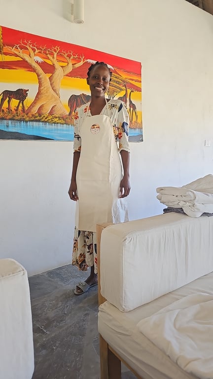 Catherine smiling in her GeGi apron beside a colourful African landscape painting