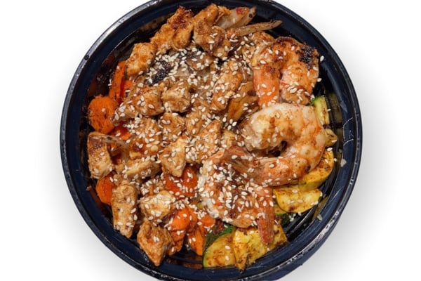 Overhead view of a takeaway bowl of sesame-topped hibachi chicken and shrimp with carrots and zucchini