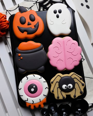 Tray of iced Halloween cookies shaped like a jack-o'-lantern, a ghost, a cauldron, a brain, an eyeball and a spider