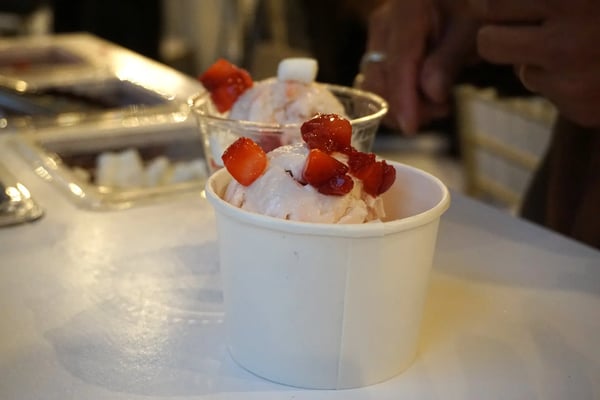 Paper cup of strawberry ice cream topped with chopped strawberries, with a second cup behind it