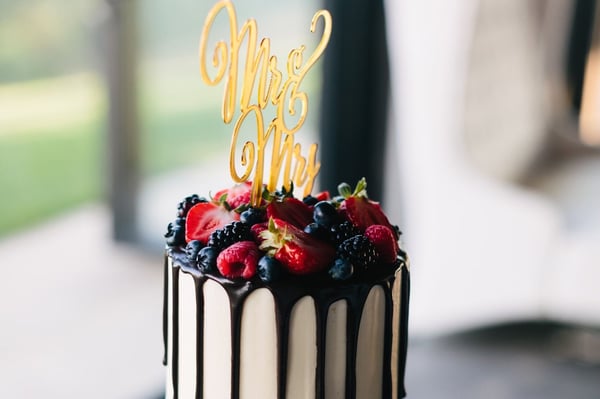 Drip cake with dark chocolate drizzle topped with strawberries and berries and a gold Mr and Mrs cake topper