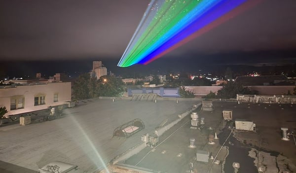 Rainbow sky laser beam fanning out above city rooftops at night