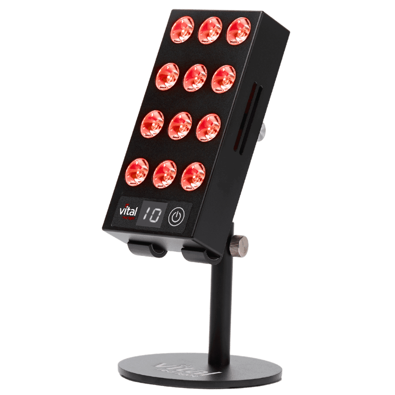 Vital Red LIght. Red Light Therapy. A handheld red light therapy device with 12 illuminated LEDs, vital charge digital display, and a round base stand, shown against a plain light background.