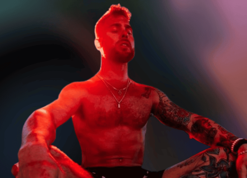 A person sits cross-legged in a meditative pose, eyes closed, amid a scene bathed in red and black lighting. The atmosphere hints at the benefits of red light therapy, with tattoos and accessories subtly highlighted by the glow.
