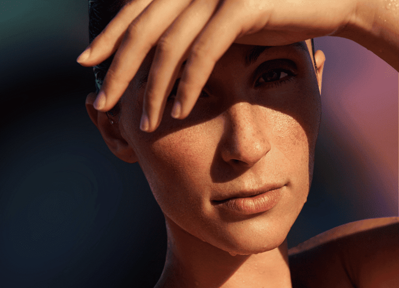 A person shading their eyes from sunlight with a hand, their face revealing soft shadows. This careful protection is reminiscent of the benefits of red light therapy for skin health and anti-aging, highlighting the importance of caring for one's complexion.