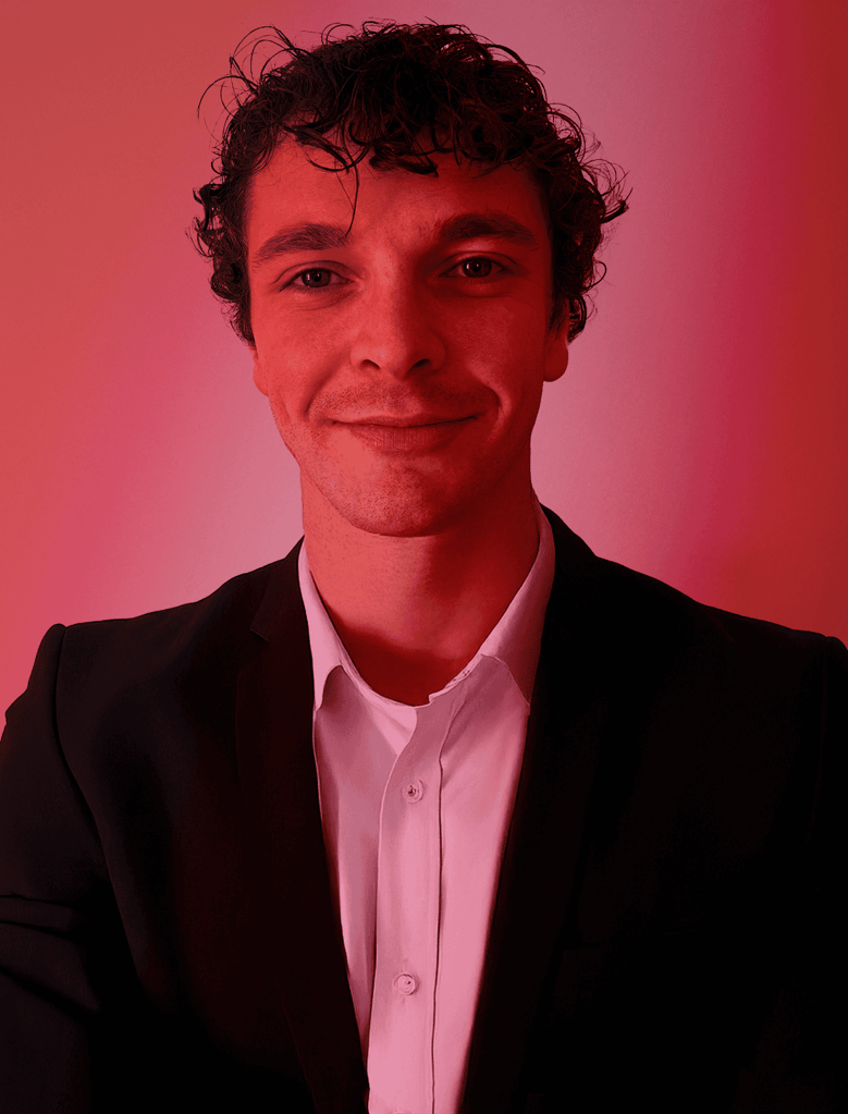 Against a vibrant red-lit backdrop, a person with curly hair in a white shirt and dark jacket offers a slight smile at the camera, embodying the welcoming spirit of our "About Us" ethos.
