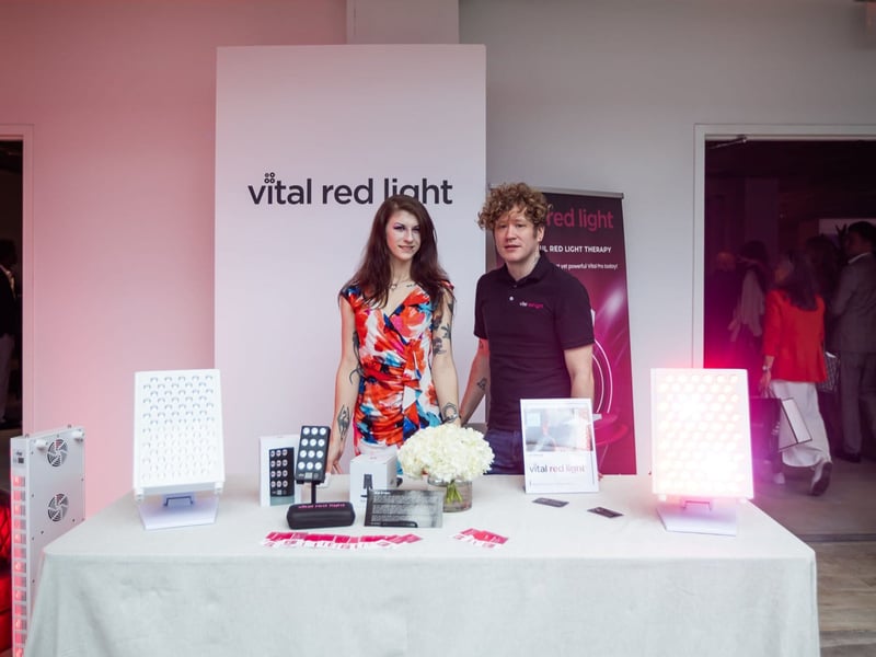 Two individuals stand proudly behind a display table featuring Vital Red Light products and promotional materials, basking in the excitement of the New You Awards.