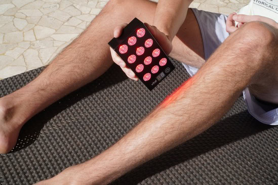 A man using the Vital Charge red light therapy device on his legs and feet