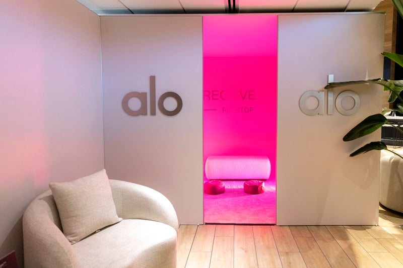 Vital Red LIght. Red Light Therapy. A minimalist lounge area with a cushioned chair and pink lighting, featuring the "alo" logo and "RECOVERY PIT STOP" on the wall—part of a Wellness Activation at the Miami Grand Prix 2025 with Vital Red Light elements.