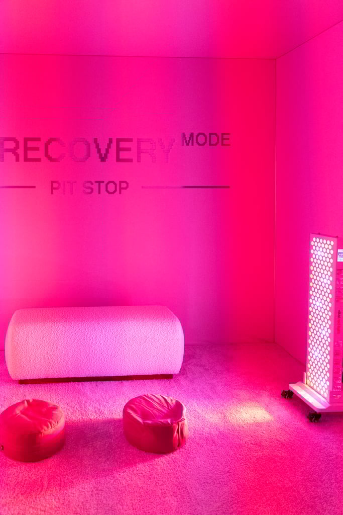 Vital Red LIght. Red Light Therapy. A room lit with pink light featuring a cylindrical bench, two round cushions, a Vital Red Light therapy panel, and "RECOVERY MODE PIT STOP" on the wall—perfect for a wellness activation at the Miami Grand Prix 2025.