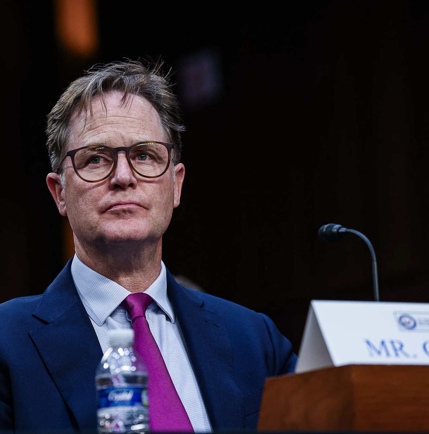 TechDogs-"Ex-Meta Exec Says Artists Will "Kill” The AI Industry"-"Nick Clegg At A Hearing, Wearing Glasses And A Blue Suit With Magenta Tie, Seated Behind A Microphone At The Charleston Festival."