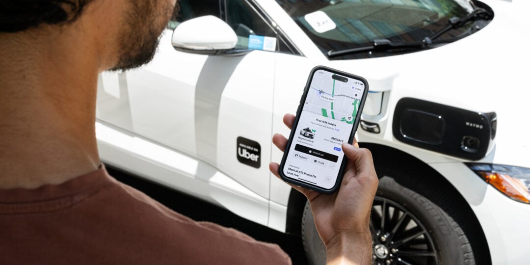 TechDogs-"An Image Of A Person Using The Uber App On A Phone To Book A Waymo Robotaxi"