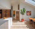 Preview of Ainslie Remodel and Addition - Image 7: kitchen, light wood floor, indoor plants, skylight, open floor plan, dining area, modern design, wood cabinetry, wooden furniture, white countertops, natural light, wall art.