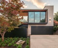 Preview of Ainslie Remodel and Addition - Image 1: modern house, large windows, wood cladding, concrete driveway, exterior lighting, landscaping, single-family home, flat roof, minimalistic design.