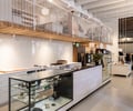 Preview of Flora and Henri - Image 2: store interior, mezzanine, glass display, wood accents, white cabinetry, black countertop, pendant lighting, open ceiling, structure wood, board ceiling, interior lighting, retail design, product display, modern design, industrial style, clean lines, contemporary finishes.