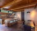 Preview of Vashon Island Cabin - Image 8: kitchen, wood ceiling, wood paneling, track lighting, glass table, bar stools, pendant lights, natural light, modern, contemporary, minimalist, open shelving, indoor-outdoor connection, greenery, counter seating, wooden beams, dining area, concrete floor, stainless steel appliances.