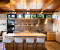Preview of Vashon Island Cabin - Image 12: kitchen, modern, wood ceiling, exposed beams, pendant lighting, stainless steel, neutral tones, open shelving, large windows, natural light, wood cabinetry, minimalist, industrial, concrete floor, bar seating, wooden accents, built-in appliances.