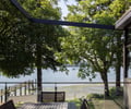 Preview of Vashon Island Cabin - Image 14: deck, outdoor seating, waterfront, glass railing, wooden ceiling, steel frame, modern, contemporary, outdoor dining, natural light, landscape design, trees, lake view, minimalist, patio, exterior space, architecture, scenic view, architectural design.