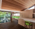 Preview of KITCHEN CONNECTED - Image 1: kitchen, wood paneling, large windows, natural light, wooden ceiling, pendant lighting, open space, wood cabinetry, countertop, modern design, green accent, built-in seating, seamless integration, indoor-outdoor connection, warm tones, minimalist decor, wood flooring, contemporary style.
