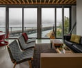 Preview of Lagerberg Mooring - Image 21: waterfront, concrete floor, concrete wall, large windows, steel frame, open plan, rug, wood accents, contemporary, modern furniture, living area, natural light, ceiling beams, indoor-outdoor connection, glass doors, metal frame chairs, minimalist, urban, seating area, view, patio, interior design, architecture, modern design, waterfront.