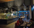 Preview of Mamnoon Restaurant - Image 10: Dining Room, Dining table, Kitchen, Steel, Concrete, Wood, Glass, Window, Sliding Door, Glass Door, Stainless Steel, Tile, Restaurant, Entry, Exposed Structure, Structure Steel.