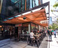Preview of Mamnoon Street - Image 4: Restaurant, steel, Wood, Concrete, Glass, Window, Storefront, Entry, Door, Dining Table, Outdoor, Street.