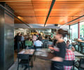 Preview of Mamnoon Street - Image 5: Person, Dining Table, Bench, Wood, Steel, Concrete, Bar, Kitchen, Glass, Window, Storefront, Restaurant.