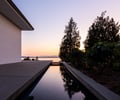 Preview of Northwest Reflections - Image 1: Roland Terry, concrete deck, reflective water feature, modern architecture, minimal design, concrete patio, evening light, outdoor space, landscape design, horizon view, wooden slats, natural setting, geometric lines, sunset backdrop.