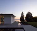 Preview of Northwest Reflections - Image 3: Roland Terry, modern architecture, flat roof, large windows, sliding glass door, concrete patio, water feature, minimalist design, open plan, landscape integration, outdoor lighting, garden, glass facade, sunset view, outdoor seating, contemporary style, glass railing.